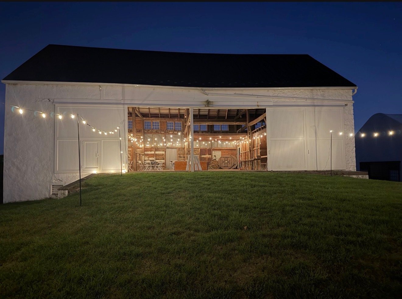 The White Bank Barn at night, doors open, lit with string lights